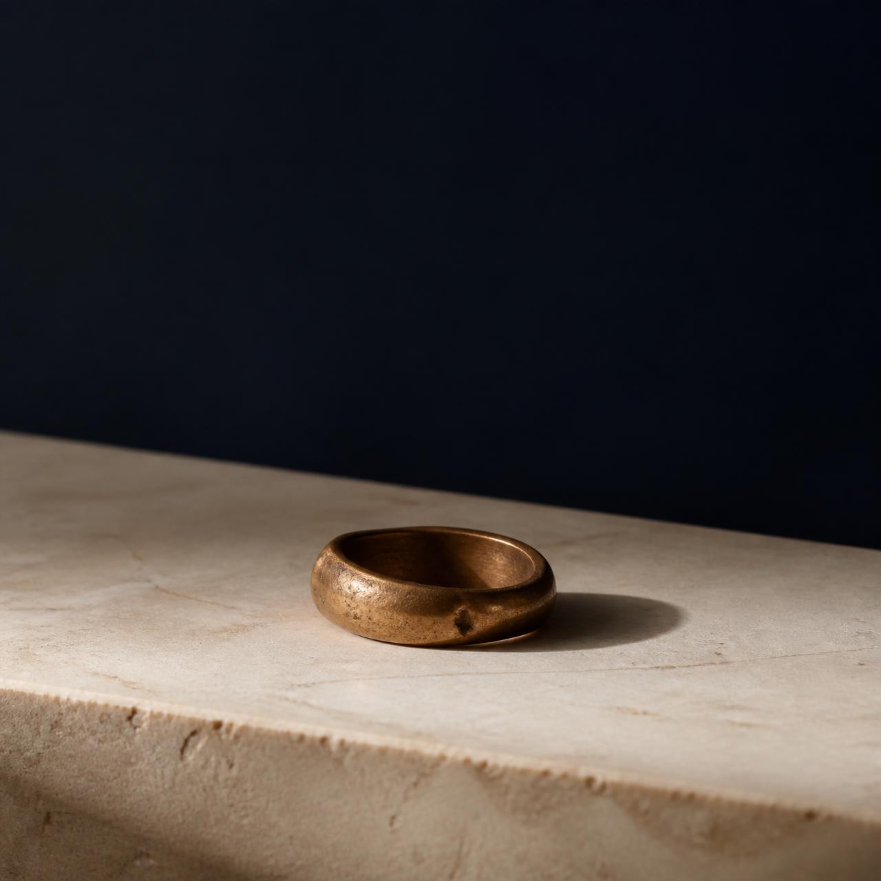 A single hand-cast bronze ring resting on warm stone — a symbol of the Collective.